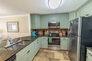 Eine Küche mit hellgrünen Schränken, einem Edelstahlkühlschrank, einer Mikrowelle, einem Backofen und einer Arbeitsplatte aus Granit.