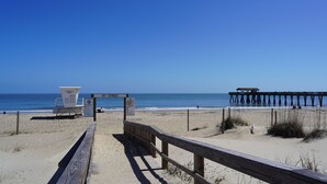 A wooden boardwalk leading to a beach with a lifeguard stand and a pier in the background. - Spacious 3-bedroom condo in the heart of Tybee Island. Easy beach access. (Tybee Island)