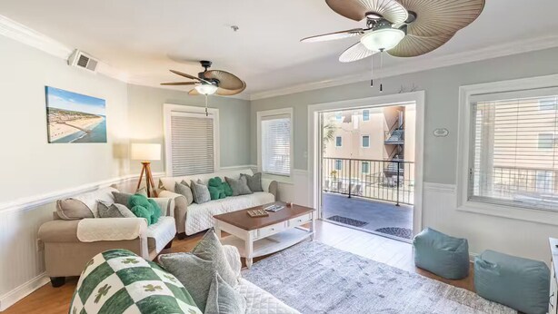 A spacious living room with a sofa, coffee table, and two accent chairs. There are ceiling fans, a large window, and a view of the outside. - Spacious 3-bedroom condo in the heart of Tybee Island. Easy beach access. (Tybee Island)