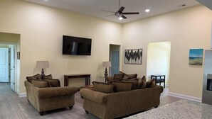 A living room with two brown sofas, a flat-screen TV, a ceiling fan, and artwork on the walls. - Superb 4-bedroom house with AC in charming Loris (Loris)