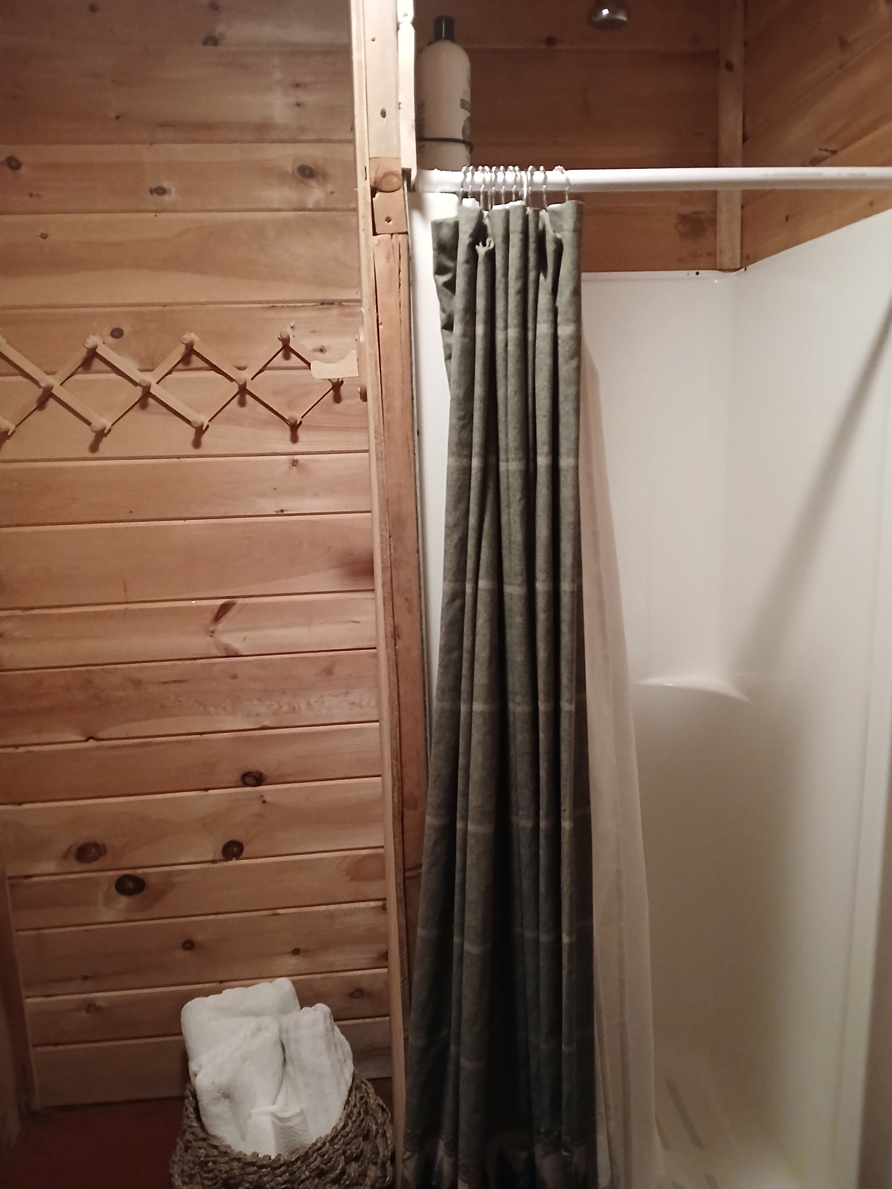 Ein Holzhütten-Interieur mit Duschbereich, einem hängenden Handtuchhalter und einer weißen Flasche an der Wand.