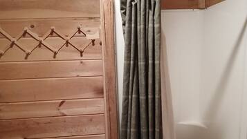 Ein Holzhütten-Interieur mit Duschbereich, einem hängenden Handtuchhalter und einer weißen Flasche an der Wand.