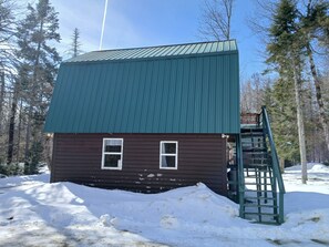 Une petite cabane avec un toit vert, une façade en bois et un petit escalier menant à une terrasse.