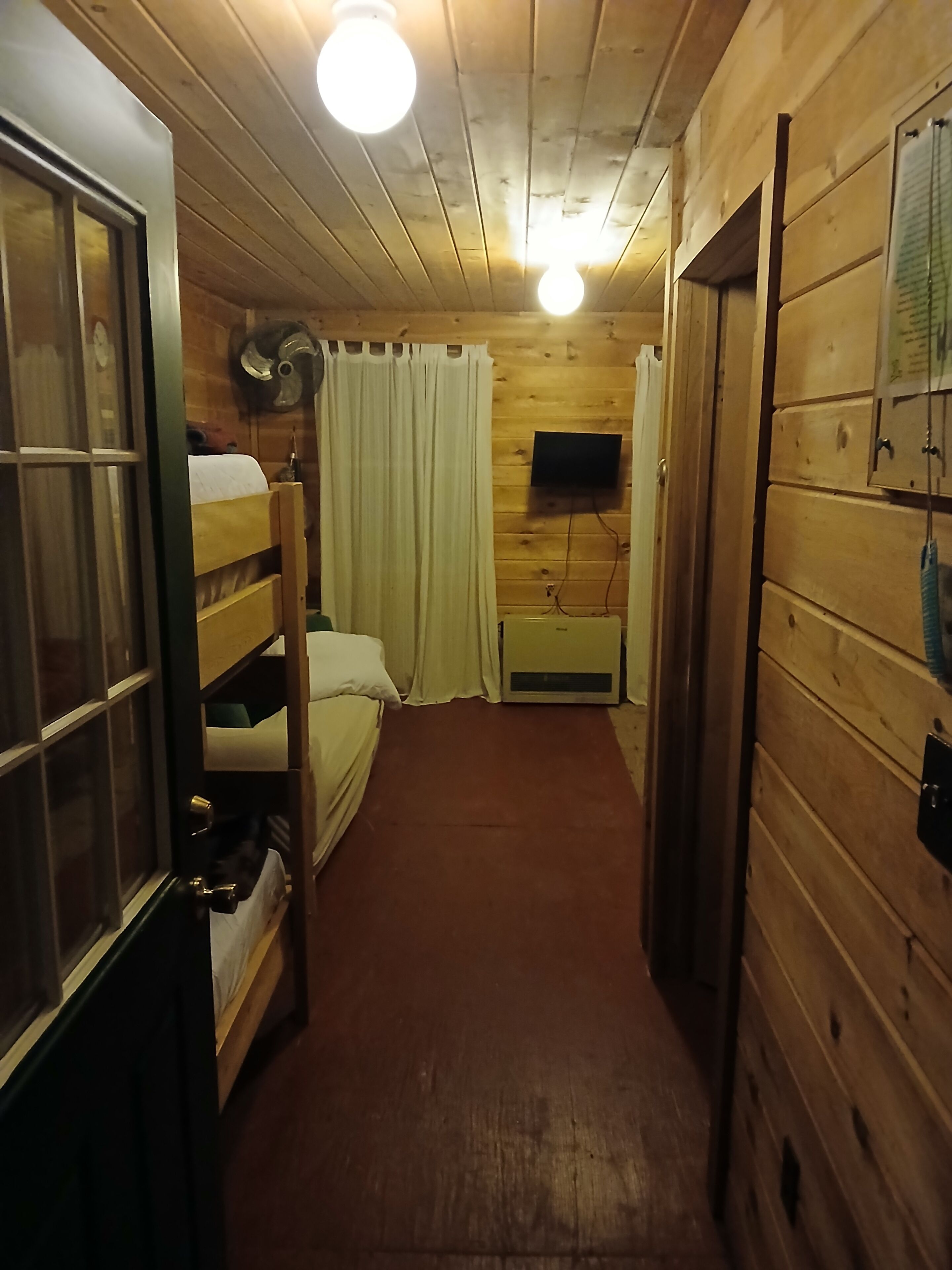 Een smalle gang met houten wanden, een stapelbed, een flatscreen televisie aan de muur en een plafondventilator.