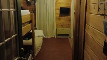 Een smalle gang met houten wanden, een stapelbed, een flatscreen televisie aan de muur en een plafondventilator.