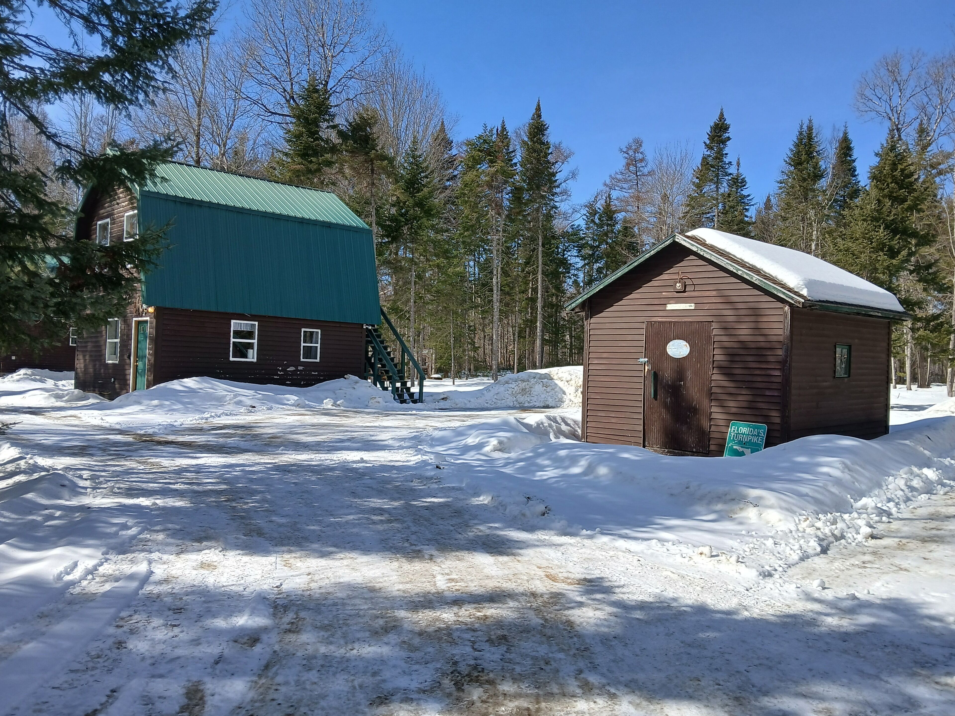 A cabin with a green roof and a small wooden structure with a snow-covered roof.