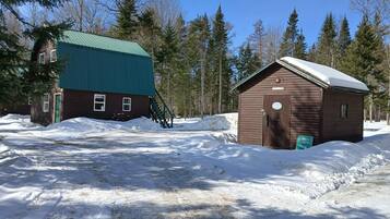 A cabin with a green roof and a small wooden structure with a snow-covered roof.