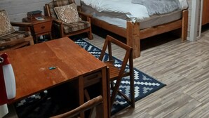 Una habitación con una cama de madera, dos sillas, una mesita y una ventana con cortinas.