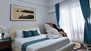 Hotellihuone, jossa on suuri sänky, yöpöytä, seinälle asennettu ilmastointilaite, ikkuna verhoilla ja seinällä taulu.