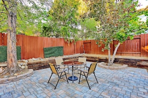 An outdoor patio with a round table and chairs, surrounded by a brick floor and a wooden fence.