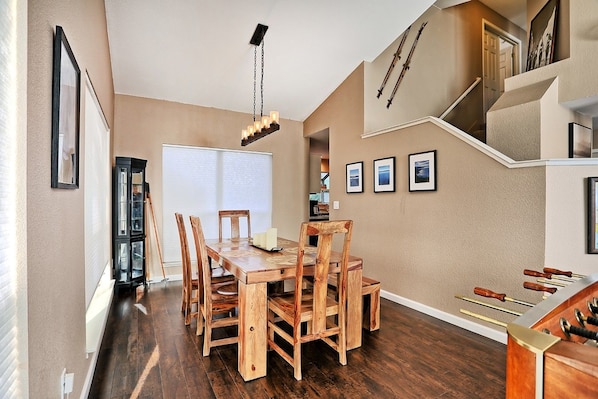 A dining area with a wooden table and chairs, a chandelier, and a staircase with a ski rack.