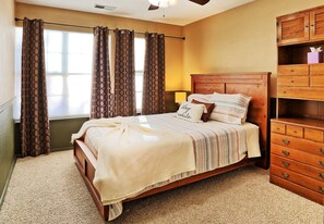 A bedroom with a wooden bed, a bedside lamp, a dresser, and patterned curtains.