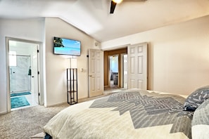 A bedroom with a large bed, a TV mounted on the wall, and a door leading to a bathroom.
