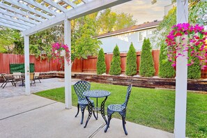 Un patio exterior con pérgola, una mesa redonda y dos sillas.