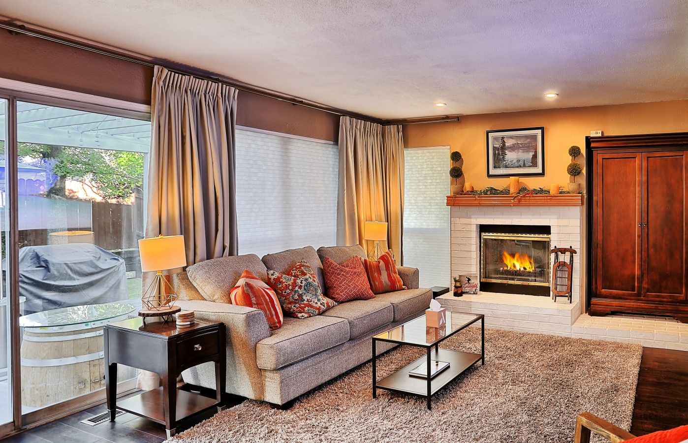 A living room with a sofa, coffee table, fireplace, and a view through large windows.