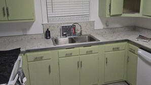 A kitchen with green cabinets, a double sink, and a window with blinds. - Serene vintage 3b/2ba  home with AC. Medical professions MD, NP, RN are welcome. (Valdosta)