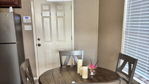 A kitchen with a round wooden table, four chairs, a refrigerator, a door, and a window with blinds. - Blue Cottage with a garden tub. Walking distance to TCU. Near the Zoo & Dickies (Fort Worth)