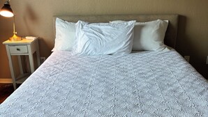 A neatly made bed with a textured white bedspread, a bedside lamp, and a nightstand with a drawer. - Blue Cottage with a garden tub. Walking distance to TCU. Near the Zoo & Dickies (Fort Worth)