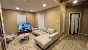 A living room with a sectional sofa, a coffee table, and a television. - Blue Cottage with a garden tub. Walking distance to TCU. Near the Zoo & Dickies (Fort Worth)
