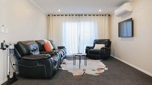 Ein modernes Wohnzimmer mit einer Ledersofa, einem Ledersessel, einem kleinen runden Tisch und einem Kuhfellteppich.