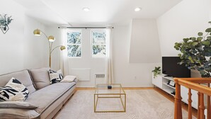 Uma sala de estar moderna com sofá, mesa de centro de vidro, televisão e escada.