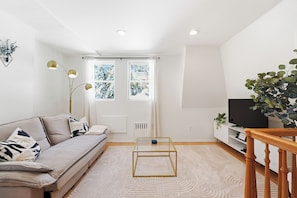 Ein modernes Wohnzimmer mit einer Couch, einem Glastisch, einem Fernseher und einer Treppe.