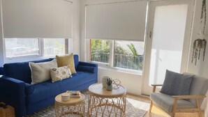 A living room with a blue sofa, two round wooden tables, and a grey armchair. - A Cozy 1BR in Cronulla – Walk to Beach & Shops U4 (Cronulla)