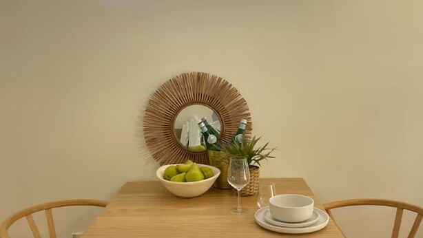 A dining table with a neon sign reading "Cronulla," a bowl of green apples, a glass, and a white bowl on a white plate. - A Cozy 1BR in Cronulla – Walk to Beach & Shops U4 (Cronulla)