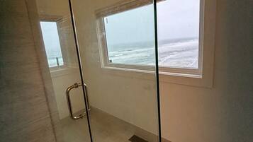 Une salle de bain moderne dotée d’une douche à parois de verre, d’une petite fenêtre donnant sur l’océan et d’un sol décoré d’un motif en chevrons.