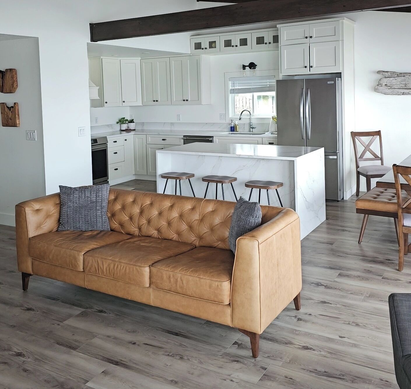 A modern kitchen with white cabinets, a stainless steel refrigerator, and a marble island with bar stools.