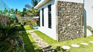 Uma casa moderna com parede de pedra, piscina e jardim bem cuidado.