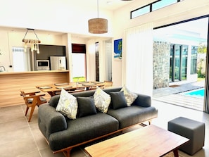 Ein modernes Wohnzimmer mit grauem Sofa, Couchtisch aus Holz und einem Essbereich mit Holztisch und Stühlen.