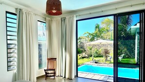 Quarto com uma cama grande, uma cadeira, vista para uma piscina e varanda com vista para o exterior.
