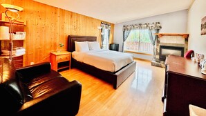 Habitación de hotel con pared de madera, una cama, una mesita de noche, un escritorio, una silla, chimenea y una ventana con cortinas.