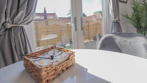 Ein Zimmer mit einem weißen Tisch, einem gewebten Korb mit Nadel und Faden und Blick auf einen Holzzaun und ein Gebäude draußen.