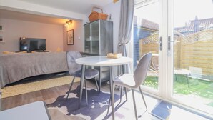 Ein gemütliches Zimmer mit Sofa, Fernseher, eine Glasvitrine, einem Esstisch mit Stühlen und einer Glastür zu einer Terrasse.
