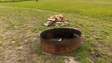 Un foyer en métal avec des bûches, situé dans un champ d’herbe.
