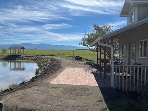 A house with a covered porch, a brick pathway leading to a pond, and a view of distant mountains.