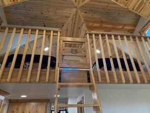 Un interior de madera con cama estilo loft, una escalera de madera y un techo con vigas a la vista.