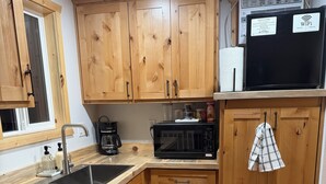 Eine Küche mit Holzausstattung, einer Mikrowelle, einer Kaffeemaschine und einem Spülbecken.
