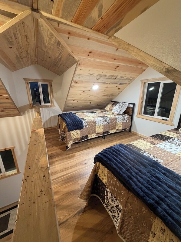 A loft bedroom with wooden beams, two beds, and a sloped ceiling.