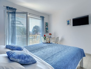 A bedroom with a bed, a TV, a table with a vase of flowers, and a view of the outside. - Villa Canaria studio by Interhome (Pula)