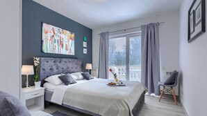 Un dormitorio moderno con una cama grande, mesitas de noche, una silla, una ventana con cortinas y un cuadro abstracto y colorido en la pared.