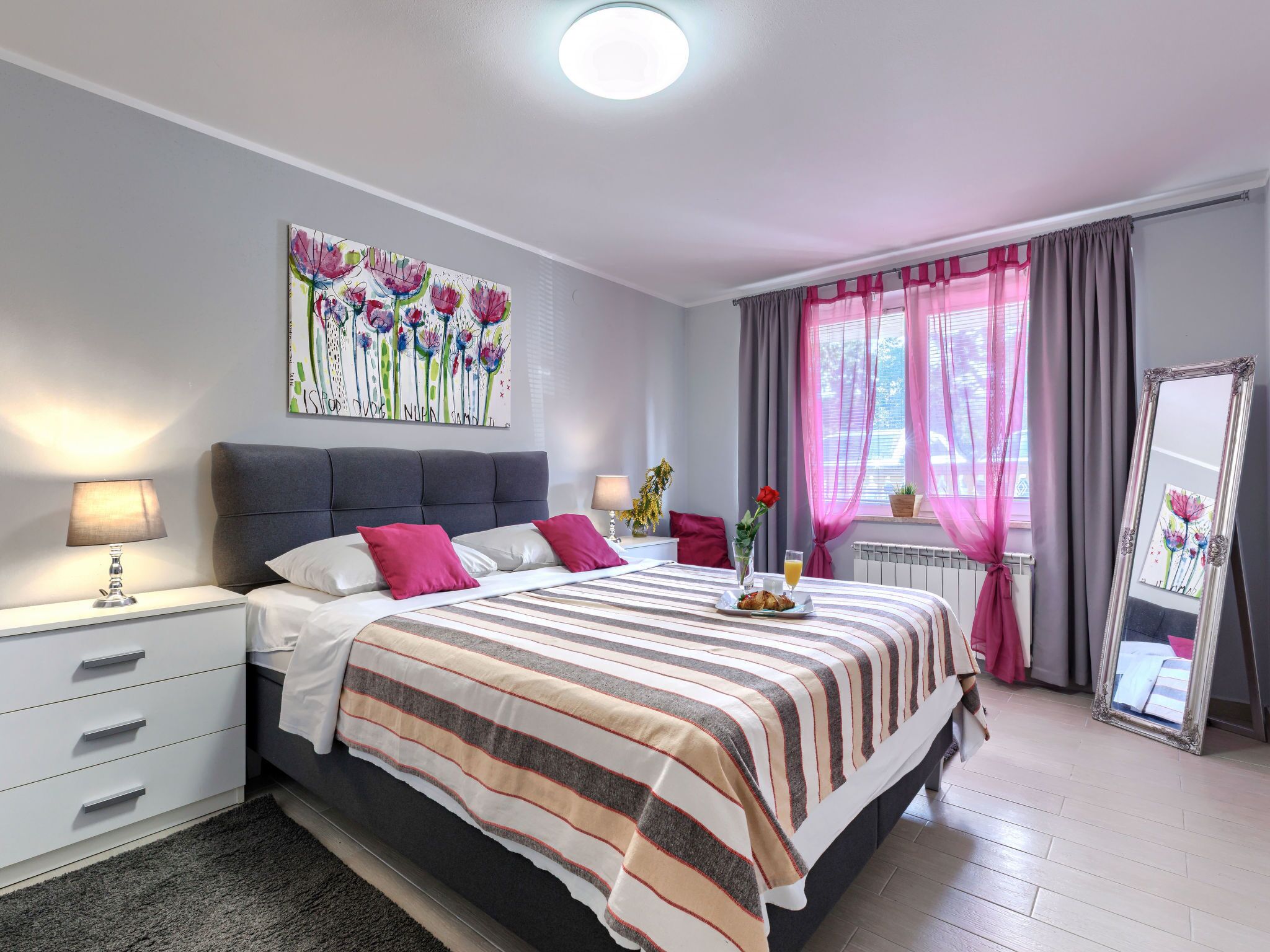 Een moderne slaapkamer met een bed, nachtkastjes, een spiegel en een raam met gordijnen.