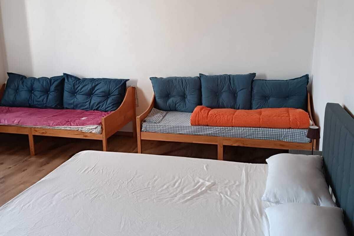 Ein Zimmer mit einem großen Bett, zwei kleineren Betten mit unterschiedlicher Bettwäsche und einer Holzbalkendecke.