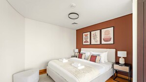 A modern hotel room with a large bed, a bedside table with a lamp, and a small white ottoman. - Silkhaus Cozy Studio With Difc Views (Dubai)