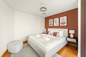 A modern hotel room with a large bed, a bedside table with a lamp, and a small white ottoman. - Silkhaus Cozy Studio With Difc Views (Dubai)