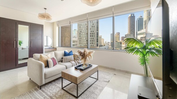 A modern living room with a sofa, coffee table, and large windows offering a city view. - Silkhaus Cozy Studio With Difc Views (Dubai)