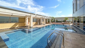 A modern outdoor swimming pool with clear blue tiles, a metal safety railing, and a view of a cityscape through large windows. - Silkhaus Cozy Studio With Difc Views (Dubai)