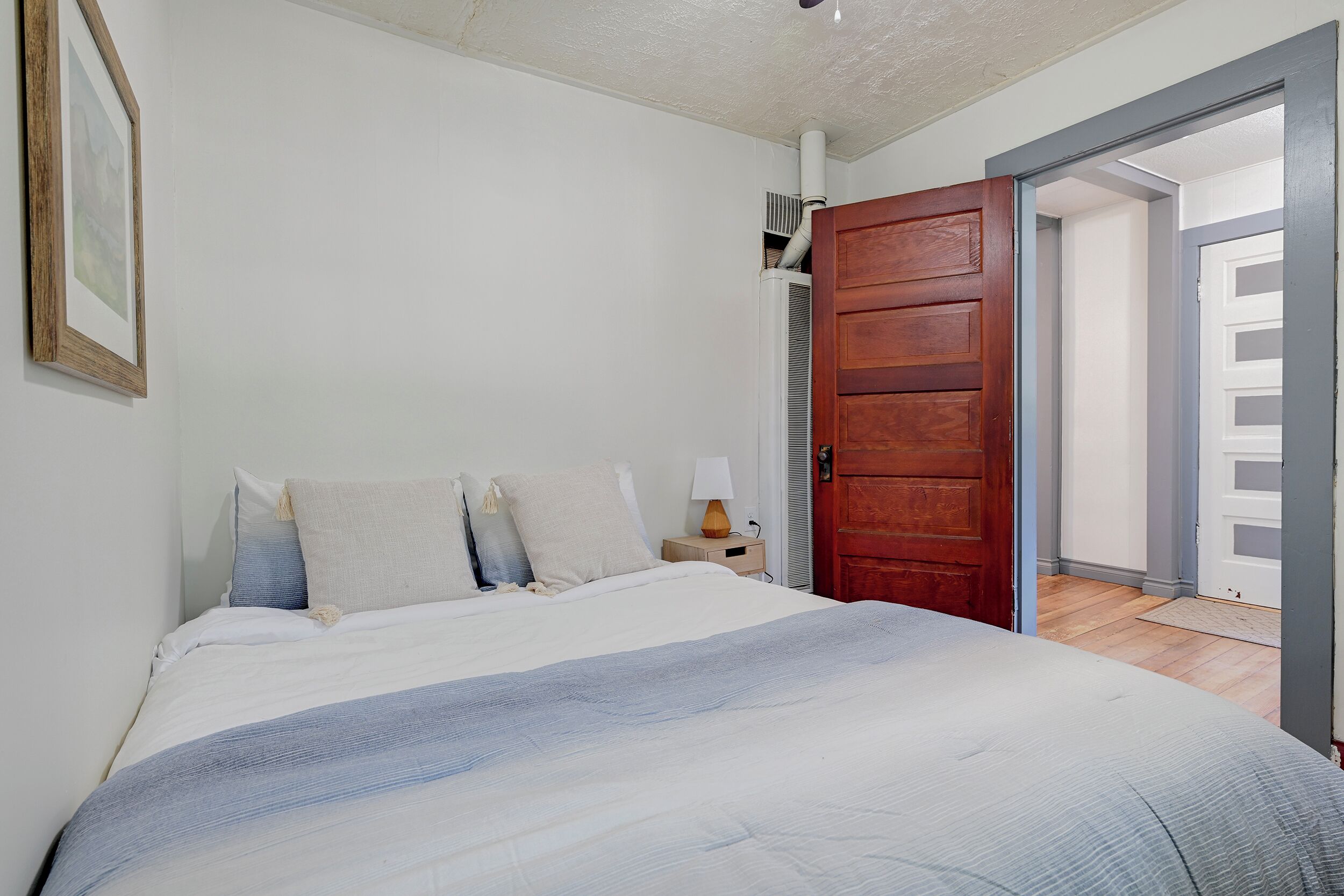 A bedroom with a bed, a nightstand, a wooden door, and an open door leading to another room.